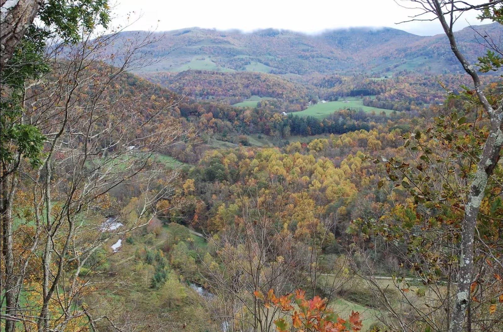 The valley seen from the ridge above — fields, the house, and the white barn tucked below